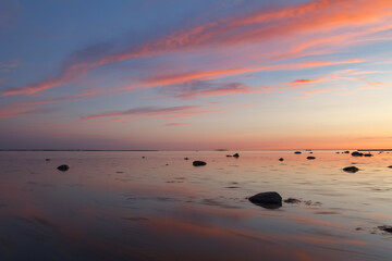 Sunset with a beutiful pink colored clouds. Long exposure photo of rocky sea shore in the evening