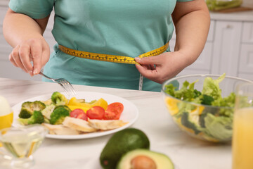 Overweight woman measuring waist while having meal at home, closeup