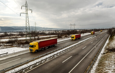 Fototapeta premium Convoy of Transportation Lorry Trucks on a Highway in a snowy winter landscape. Business Transportation And Trucking Industry.