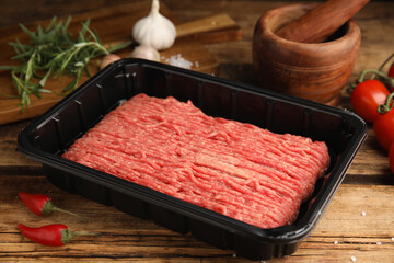 Raw fresh minced meat in plastic container and other ingredients on wooden table