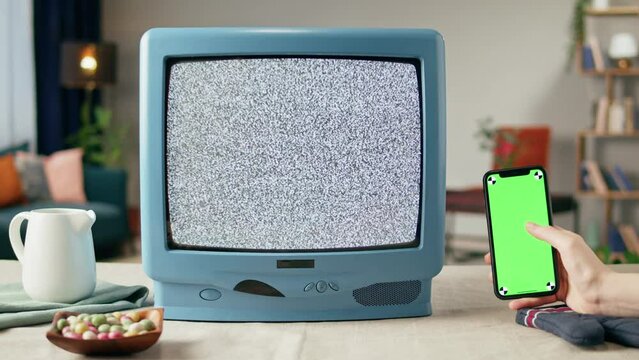 Old television with grey blank screen on home background living room, using smartphone with chroma key. Close-up of vintage tv on kitchen table, nostalgia.