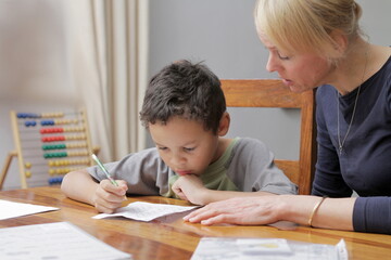 boy child doing homework learning at home with mother sitting at a table stock photo