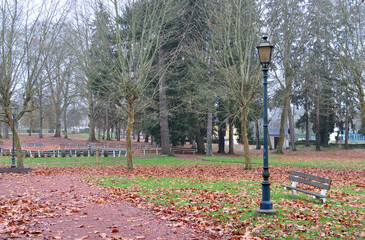 Old Lamp Post and Bench in Deserted Public Park with Autumnal Trees