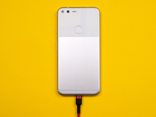 Smartphone is connected to a charger to charge the battery on a colored background