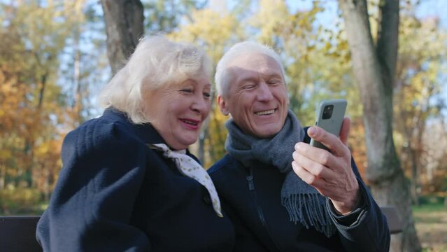 Cheerful senior couple laughing, watching funny videos in social media on phone