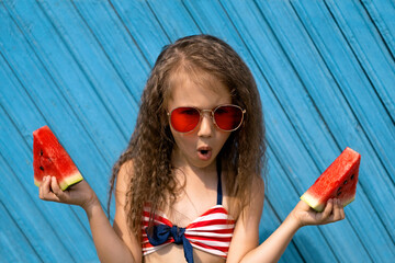 A curly-haired brunette girl with an open mouth from indignation holds two pieces of fresh juicy watermelon in hands. Refreshing berry-fruit taste.