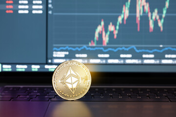 Ethereum coin on laptop and chart on display at background. Cryptocurrency trading or investment concept