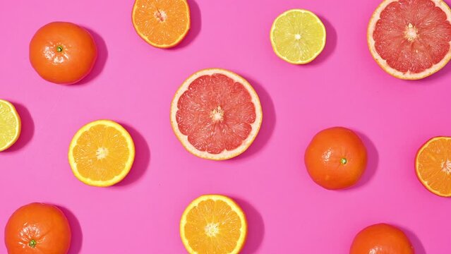Citrus fruits appear from the center and making pattern on vibrant pink theme. Stop motion flat lay