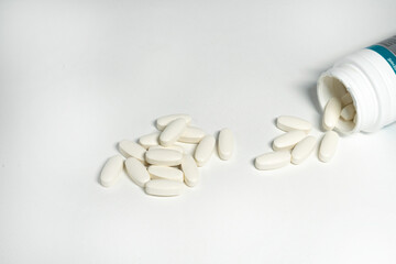 Bottle with white oval pills in plastic container on white background