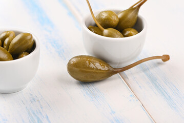 Capers in a white little bowl on the white background.
