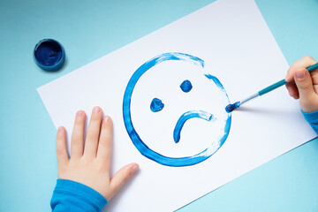 Top view of the child hands,drawing sad face.Blue monday and mental health concept.