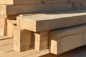 Wooden building materials close up.
A stack of natural wooden boards at a construction site. Industrial edged timber. Wooden rafters for renovation or construction. Roofing and carpentry lumber.