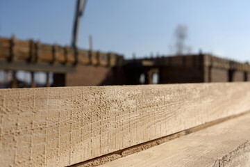 Fototapeta premium Wooden building materials close up. A stack of natural wooden boards at a construction site. Industrial edged timber. Wooden rafters for renovation or construction. Roofing and carpentry lumber.