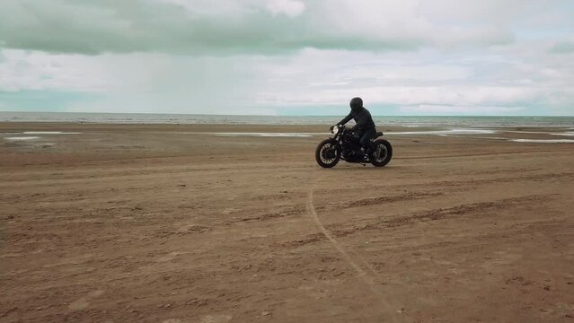 А man on a black motorcycle rides on a sandy beach.