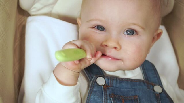 baby bites plastic spoon and looks at camera closeup