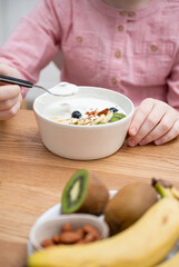 The hands of a girl in a pink shirt hold a bowl of yogurt, granola and fresh fruit on a wooden table. The concept  of healthy eating. Vertical orientation