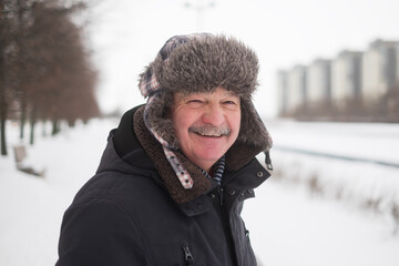 Senior man in warm hat standing in snowy outdoors.