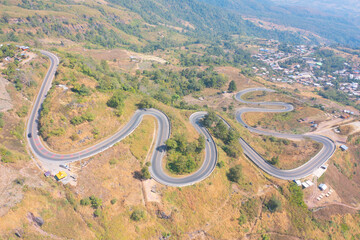 Aerial view of cars driving on curved, zigzag curve road or street on mountain hill with green natural forest trees in rural area of Nan, Thailand. Transportation.