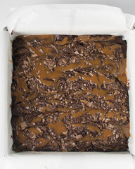 Raw brownie batter in a  lined baking tin, flatlay of brownie batter drizzled with caramel sauce