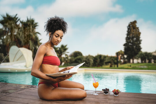 Afro American woman reading a magazine and having a fruit breakfast poolside