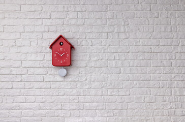 Red cuckoo bird clock with pendulum on a white brick wall background with copy space