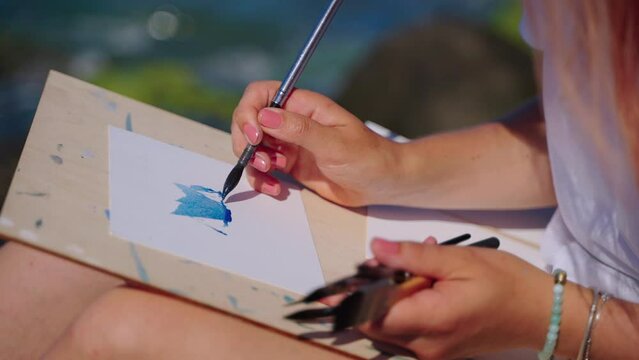 woman is drawing on seacoast, painting marine landscape from nature