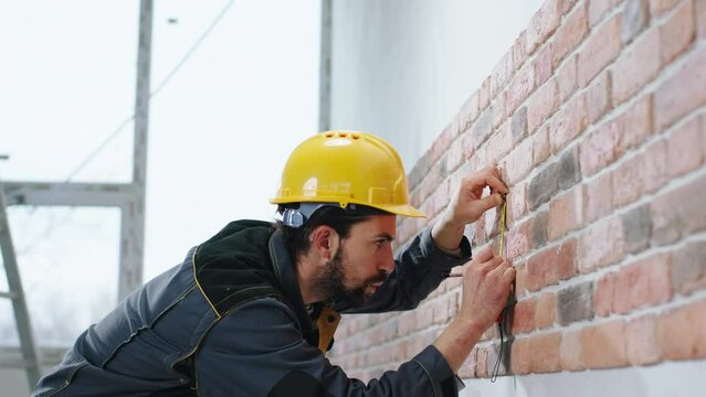 Concept of construction and architecture constructor man at construction site take measurements from a new built wall from red brick