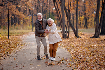 Nature season and fall holiday. Cheerful senior couple of woman and man outdoor.retired couple throwing playing with yellow tree leaves. Love relationship and romance. Couple in love in autumn park.