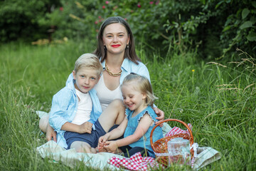 Naklejka na ściany i meble Happy mother and two children have picnic in summer park. Family, vacation and summer season concept