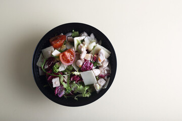 black bowl of salad isolated against light background flat lay. Image contains copy space