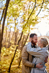 Fototapeta premium lovely couple hugging with love in the middle of park or forest during autumn at sunny day, caucasian man and woman in coats feel tenderness to each other, good relationships concept
