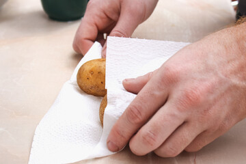 A man dries raw, washed potatoes with paper towels and napkins to bake them in foil in the oven.