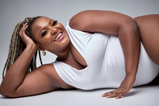 Chubby happy black woman in white bodysuit lingerie posing on