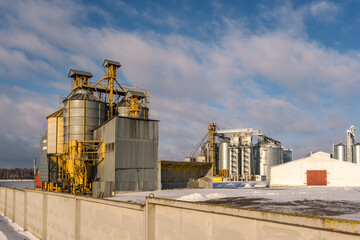 agro silos granary elevator in winter day in snowy field. Silos on agro-processing manufacturing plant for processing drying cleaning and storage of agricultural products, flour, cereals and grain.