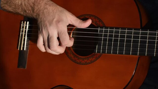 a man's hand pulls the strings on a guitar close-up