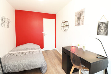 Room with a red colored wall. elephant and lion painting. A black desk with a lamp. A transparent chair. Lion and elephant paintings on the wall. (France - 15.09.2021)