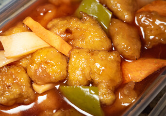 Close and selective focus on a plastic tub of Kung Po chilli chicken ordered from a Chinese takeout restaurant. With intention shallow depth of field and bokeh