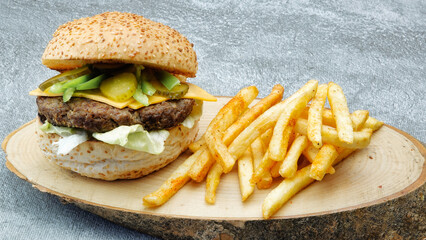 juicy cheeseburger with chili pepper, french fries, tomato, lettuce and cucumber pickle on a...
