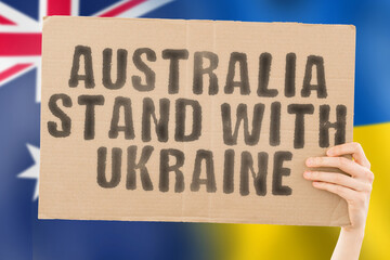 The phrase " Australia stand with Ukraine " on a banner in men's hand with blurred Australia and Ukrainian flag on the background. Team. European. War. Assistance. Negotiation. Safety. Security