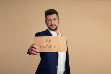 Man dressed in an elegant way, supporting the feminist movement, showing a sign saying 