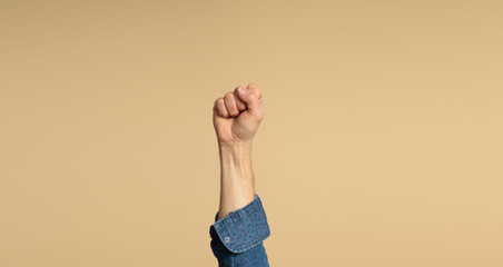 A man's hand, with a denim shirt, showing his fist, on a beige background. Feminist Movement.