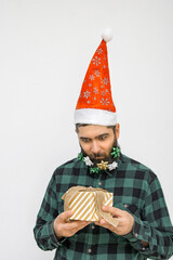 A strange man in a Santa Claus hat and with Christmas tree decorations in his beard looks greedily at the gift. Greedy Grinch. New Year's nonsense.