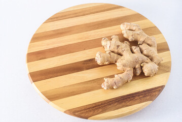 Fresh ginger root on striped round wooden board, copy space