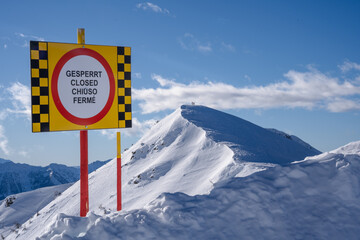 Closed ski slope sign with a snowy mountain and skier in the background