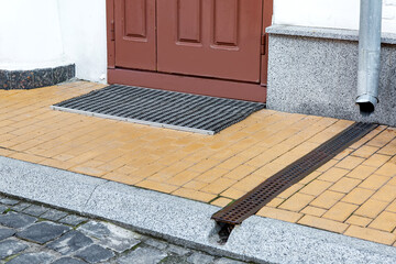Entrance door with rubber doormat of building with granite stone cladding with downspout into...