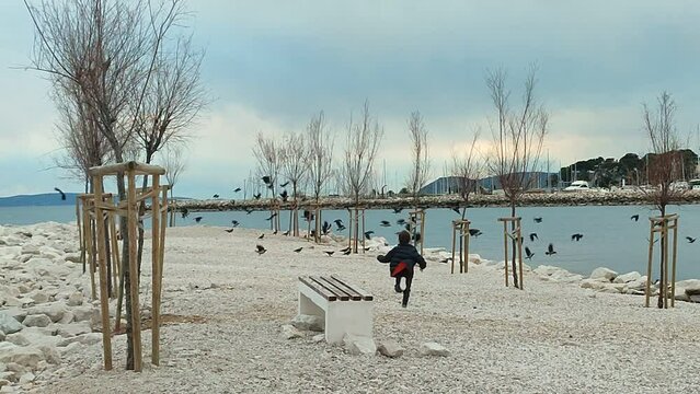 A young boy running on a beach in autumn, making a flock of birds fly away.