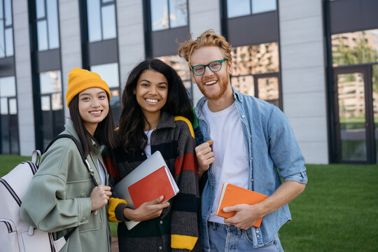 Group portrait of multiracial smiling students with books and backpacks looking at camera walking in university campus. Education concept