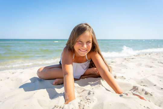 Cute little girl is sitting on the sand by the sea. Vacation.