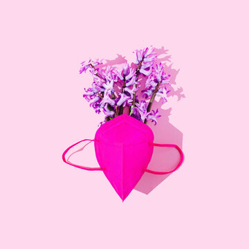A magenta protective mask and a bouquet of yacinth flowers on pink background. Creative concept for spring celebration banner. Design for Valentine's card. Flat lay