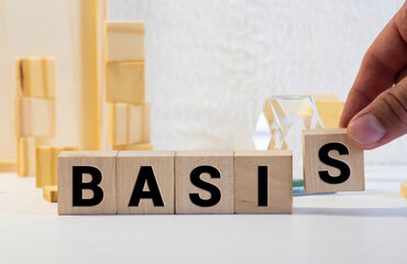 The word BASIS is written on wooden cubes lying on the office table in front of a laptop. Business...